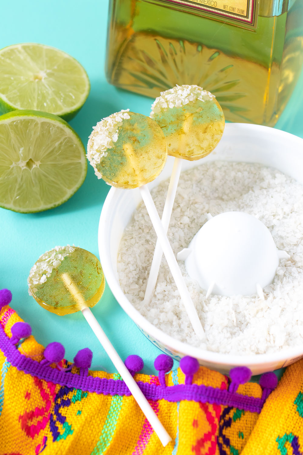 three margarita lollipops arranged in salt with bottle of tequila